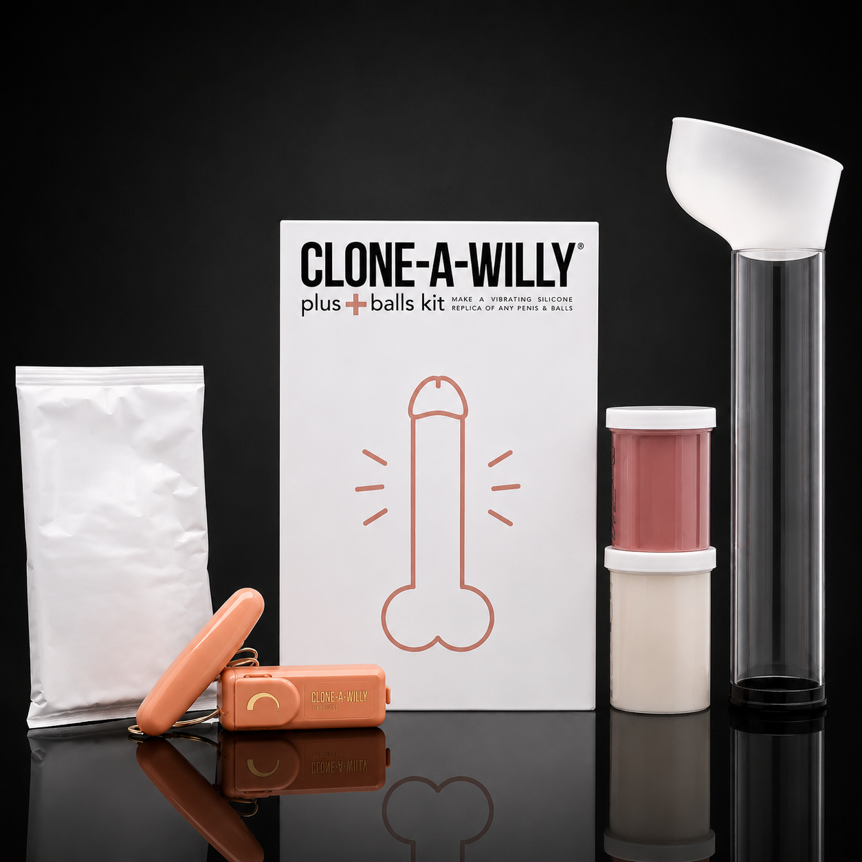 Clone-A-Willy plus balls kit displayed on a reflective black surface against a black background, including a white box with a brown outline of a penis, a white pouch, an orange cylindrical container, a pink-and-white jar, and a tall clear tube with a white funnel.