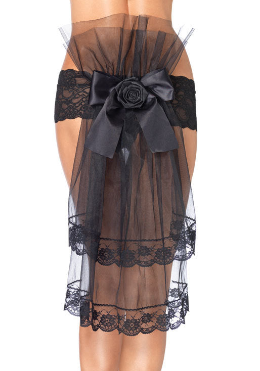 Black sheer tulle garter skirt with a large satin bow and fabric rose at the back, featuring black lace trim at the waistband and hem, shown on a model against a white background.